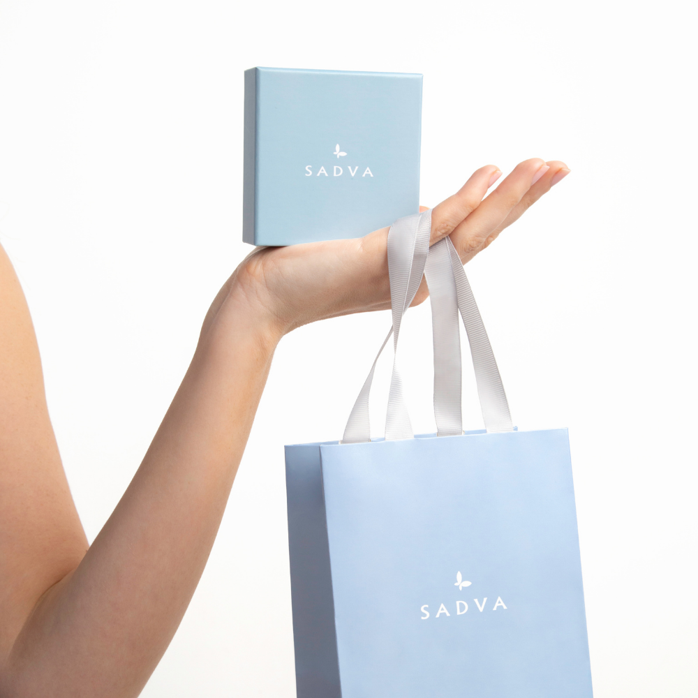 Zdjęcie przedstawia kobiecą dłoń trzymającą torebkę prezentową z logo SADVA oraz pudełko na biżuterię w kolorze baby blue.